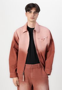Denim jacket with a gradient from light to dark reddish-pink, features a front pocket, and a zipper. Paired with matching pants.