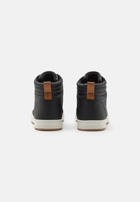 Black high-top sneakers with quilted texture, tan accent at the heel, and white rubber soles. Rear view showcases padded sides and minimal logo.
