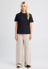 Black cotton t-shirt with a round neckline, paired with cream pinstriped wide-leg pants and black slip-on shoes. Simple design elements.