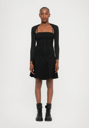 Black dress with a fitted bodice, long sleeves, and flared skirt. Features contrasting stitching and worn with black combat boots.