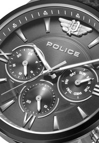 Melna analoga pulksteņa dizains ar teksturētu skalu, sudraba akcentiem, trim subskalām datuma un dienas rādīšanai, kā arī spīdīgu korpusu ar izteiksmīgiem stundu rādītājiem.