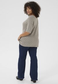 Lichtgrijze gebreide sweater met een gestructureerd, ruitpatroon en korte mouwen, gecombineerd met donkerblauwe uitlopende jeans en zwarte schoenen.