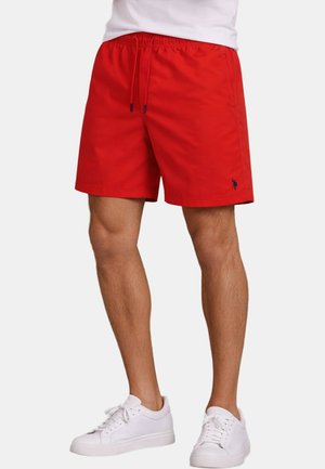 Rote Herren-Badeshorts in mittlerer Länge mit Kordelzugbund, Seitentaschen, kleinem gesticktem Logo nahe dem Saum, getragen mit weißen Sneakers.