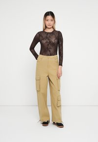 Body in pizzo marrone a maniche lunghe abbinato a pantaloni cargo color khaki chiaro con tasche laterali, design a gamba dritta e scarpe con tacco nere.