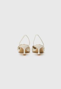 Sandales blanches à talons avec une tige synthétique lisse, un dos ouvert et un talon fin avec un accent brun clair à la base.