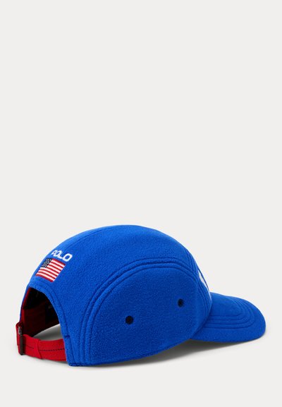Blaues Fleece-Baseballcap mit gebogenem Schirm. Mit weißem "POLO"-Schriftzug und einem Amerika-Flaggen-Patch auf der linken Seite. Roter verstellbarer Riemen.