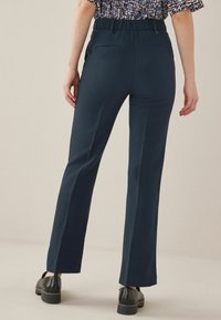 Marineblauwe rechte broek met een gladde textuur, elastische tailleband en twee achterzakken, gecombineerd met zwarte schoenen.