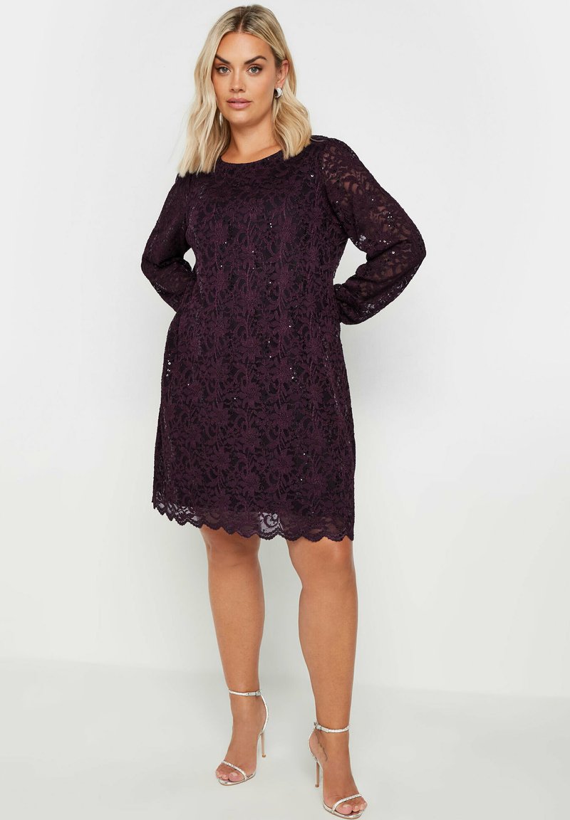 Vestido de encaje en púrpura profundo con mangas largas, dobladillo en ondas y patrón floral. Presenta un corte relajado y una textura transparente.