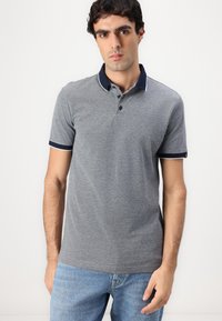 Siva polo majica s mornarsko plavim ovratnikom i manžetama, s tri gumba i teksturiranim materijalom. U kombinaciji s svijetloplavim trapericama.