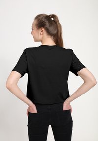 Černé tričko s krátkým rukávem vystavené zezadu, vyrobené z bavlny s volným střihem. Tkanina vypadá hladce a mírně elasticky.