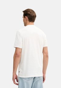 Camiseta de algodón blanca con mangas cortas, cuello redondo, textura suave y una pequeña etiqueta en la costura lateral inferior. Diseño simple y clásico.