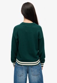 Groen gebreide trui met ronde hals, voorzien van wit- en groen gestreepte geribbelde manchetten en zoom, gedragen met lichtblauwe high-waisted jeans.