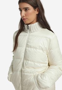 Witte donzen jas met doorgestikt ontwerp, hoge geribbelde kraag, rits aan de voorkant en zijzakken. Glad, glanzend stoffen oppervlak.