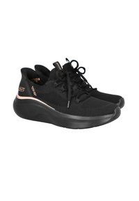 Zapatillas deportivas negras con parte superior de malla, cordones texturizados y suela acolchada. Presentan un acento metálico en el talón.