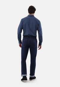 Long-sleeved blue patterned shirt, tucked into dark denim jeans with rolled cuffs and black sneakers. Back view shows sleek cut and design.