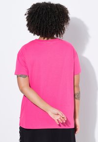 Short-sleeve, round-neck t-shirt in bright pink cotton, featuring a relaxed fit. Back view shows a smooth texture and simple design.