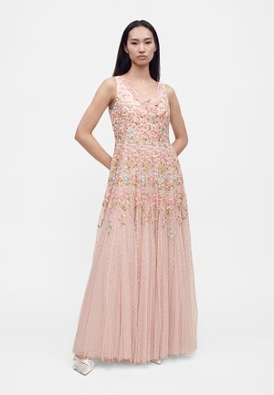 Femme portant une robe rose pâle sans manches, longue jusqu'au sol, ornée de broderies florales multicolores et de tissu tulle transparent.