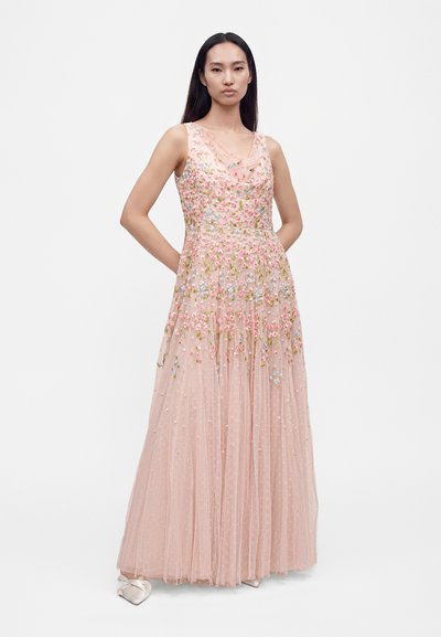 Femme portant une robe rose pâle sans manches, longue jusqu'au sol, ornée de broderies florales multicolores et de tissu tulle transparent.
