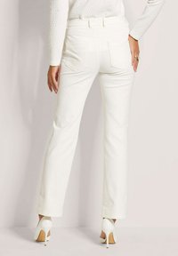 Witte rechte broek met een gladde textuur, voorzien van twee achterzakken en een hoge tailleband, gecombineerd met witte hoge hakken.