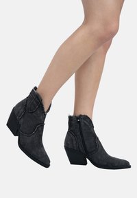 Botines de denim negro hasta el tobillo con puntera puntiaguda, cremallera lateral, bordes deshilachados y un acabado texturizado, que presentan un tacón corto y grueso.