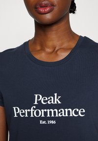 Námořnické tričko s krátkým rukávem vyrobené z bavlny, s velkým bílým potiskem "Peak Performance Est. 1986" na hrudi.