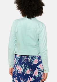 Mündroheline lühikeste varrukatega denimmantel, millel on nööbiga mansett, klassikaline disain ja nähtavad õmblusdetailid. Allpool lillemustriline seelik.