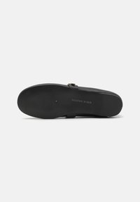 Svart sandal med teksturert såle, som har en enkel stropp og små gullspenne detaljer. Glatt materiale med minimalistisk design.