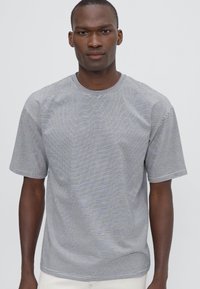 Camiseta de algodón a rayas en azul marino y blanco, con cuello redondo y mangas cortas, de corte relajado. Textura suave, diseño casual.