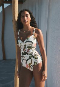 Maillot de bain une pièce floral avec une base blanche, orné de feuilles vertes et de fleurs roses, avec des bretelles réglables et un détail froncé sur le côté pour un ajustement parfait.