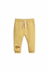 Gula bomullsbukser med elastisk midja, med en giraffapplikation och texten "HEJ VÄN?" på vänster ben. Slät textur, avslappnad design.
