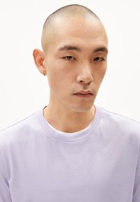 Lavenderfarbener Rundhalsausschnitt-T-Shirt mit glatter Textur. Verfügt über einen gerippten Kragen und ein minimalistisches Design. Wird über einem weißen Hemd getragen.