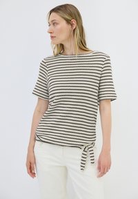Strickoberteil mit kurzen Ärmeln in Creme mit schwarzen Zickzackstreifen. Mit Rundhalsausschnitt und einem seitlichen Bindeband am Saum.