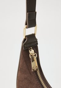 Ruske suéderi kott, katerega vogal je z zlatim zadrgo in pravokotnim obročkom, pritrjen na temno rjav usnjen trak z zlatim kovinskim obročkom.