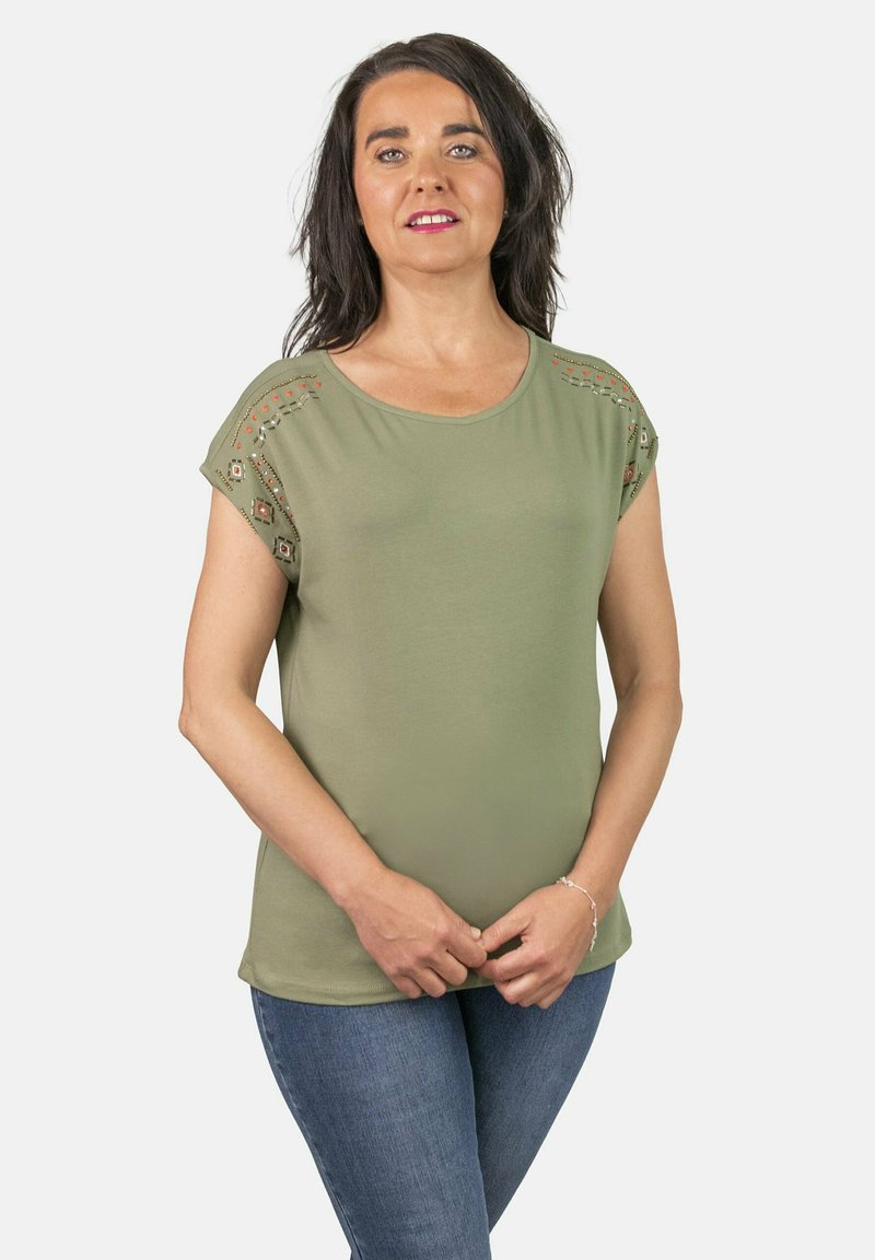 Top verde oliva de manga corta con cuello redondo, que presenta costuras decorativas y detalles recortados en los hombros, combinado con jeans de denim.