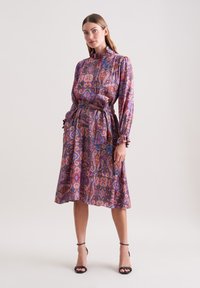 Langärmliges Kleid mit Paisleymuster in Lila-, Rosa- und Goldtönen, mit tailliertem Schnitt und Rüschensäumen. Seidige Textur.
