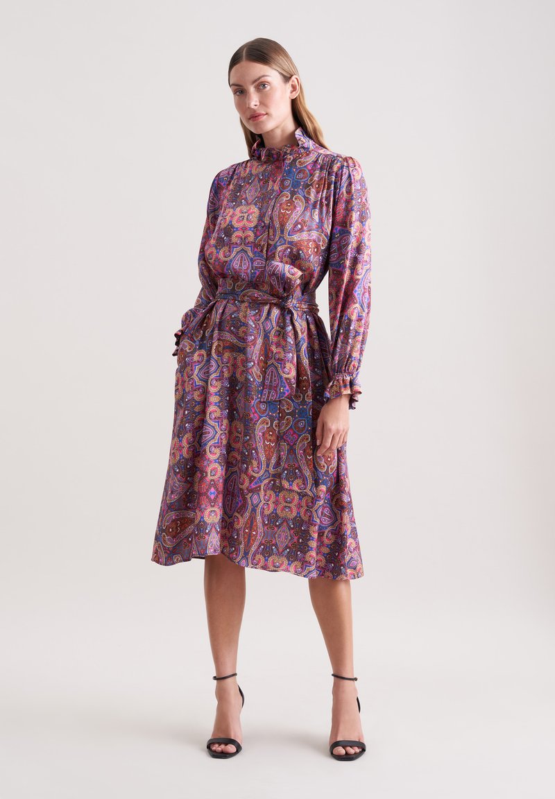 Langärmliges Kleid mit Paisleymuster in Lila-, Rosa- und Goldtönen, mit tailliertem Schnitt und Rüschensäumen. Seidige Textur.