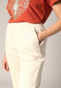 Crèmekleurige corduroy broek met verticale ribbels en een elastische tailleband, voorzien van zijzakken en een relaxte fit, gecombineerd met een rode graphic t-shirt.
