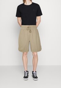 Camiseta de algodón negra, cuello redondo, mangas cortas; pantalones cortos de algodón beige con cintura elástica y cordón; zapatillas altas negras con suelas blancas.