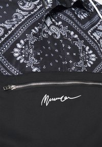 Svart och vit paisleymönstrad tyg ovanför en svart sektion med en silverdragkedja och vit skrivstilssöm nedan.