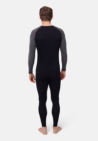 Svart värmeunderställ med långa ärmar och grå raglanärmar, parat med svarta tighta leggings. Texturerat material utan distinkta mönster.