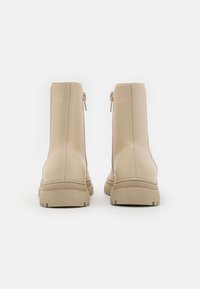 Bottes de cheville beiges en cuir lisse, avec des zips latéraux et des semelles en caoutchouc texturé, dotées d'un design à bout rond.