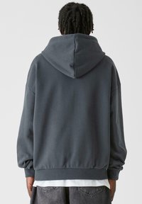Felpa oversize grigio scuro realizzata in materiale morbido, con un cappuccio ampio, polsini a costine e un orlo con vestibilità rilassata.