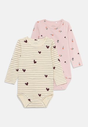 Deux bodys à manches longues pour bébé, l'un crème avec des rayures noires et des cœurs, l'autre rose avec de petits motifs floraux, sur fond blanc.