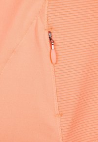 Tejido de color melocotón con textura acanalada, que presenta una cremallera plateada y un tirador de cremallera de color rosa suave. Se aprecian detalles de costura.