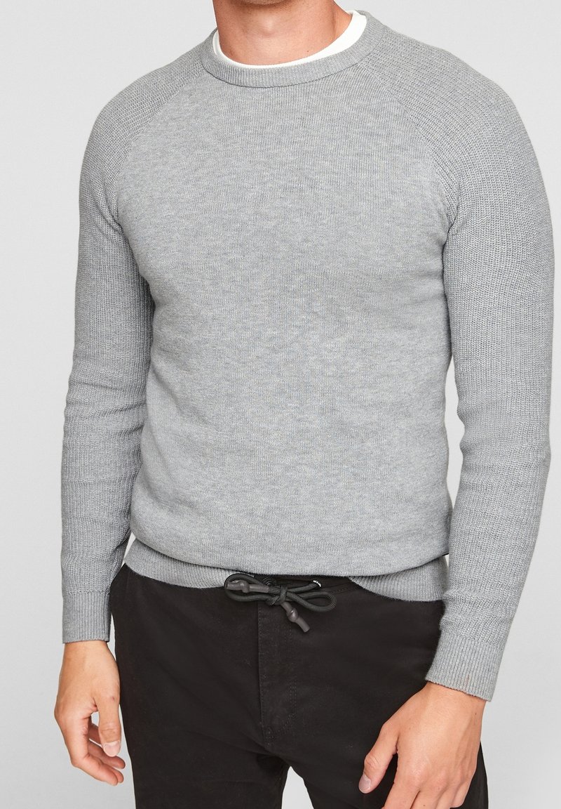Šedý pletený svetr s vroubkovou strukturou, kulatým výstřihem a raglánovými rukávy. Dokončený přiléhavým lemem a zvýrazněný stahovací šňůrkou v pase.