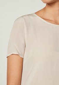 Genomskinlig crememönstrad blus med korta ärmar och rund halsringning, med en slät tygkvalitet och lätt struktur. Diskret drapering synlig.