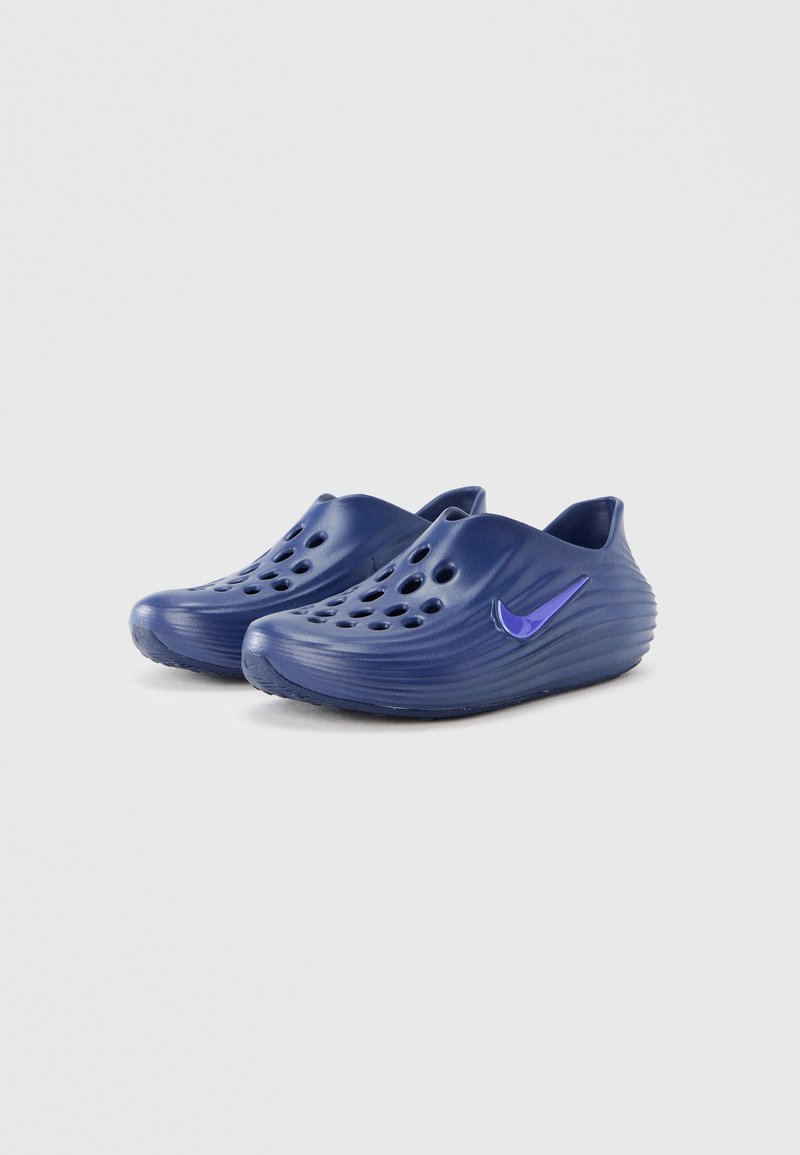 Navy blue clogs with a textured design, featuring ventilation holes and a purple Nike logo on the side. Soft, flexible material.