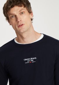 Granatowa koszulka z długim rękawem z białym logo "CROSS JEANS EST. 1990" z przodu, okrągły dekolt, gładka tekstura i luźny krój.