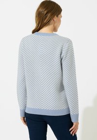 Jasnoniebieski sweter dzianinowy z wzorem w zygzaki w ciemniejszym odcieniu niebieskiego. Ściągacze na mankietach i w pasie; okrągły dekolt, teksturowany materiał.