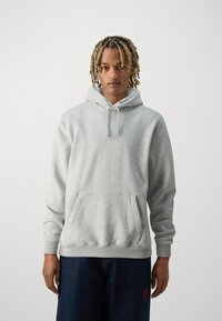 Sweat-shirt à capuche gris avec une poche avant et des poignets côtelés. Fabriqué en tissu doux et texturé, avec des cordons de serrage et une coupe décontractée.